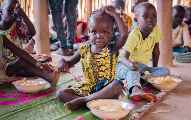 Kinder erhalten eine warme Mahlzeit in einer von der Caritas unterstützten Hilfseinrichtung © Elisabeth Sellmeier Kinder sitzen auf einer bunten Matte und essen gemeinsam in einer Hilfseinrichtung. Im Hintergrund sind weitere Kinder zu sehen