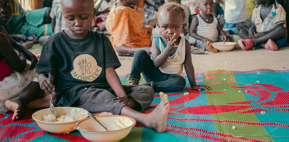 Kinder sitzen auf einer bunten Matte und essen in einem Ernährungszentrum im Südsudan.